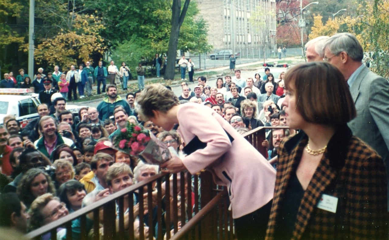 A woman stands on a raised platform, greeting a crowd assembled below