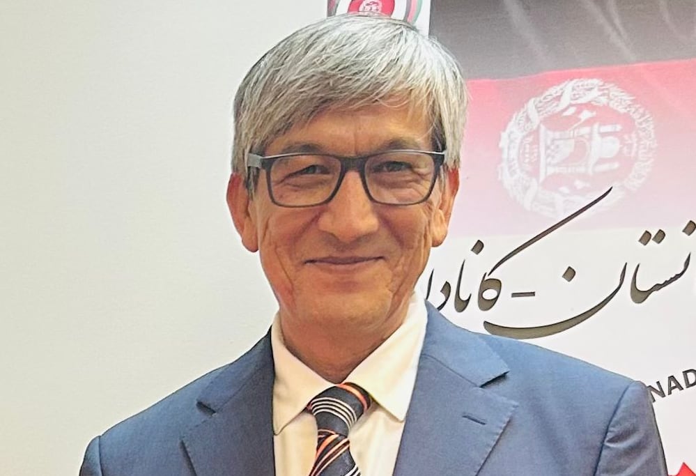 A man stands and smiles for the camera. He is wearing a suit and tie