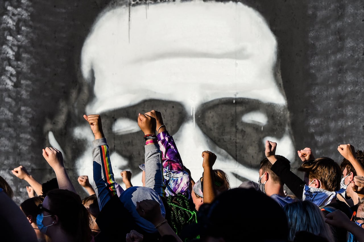 Protesters raise their hands as they gather near a mural.