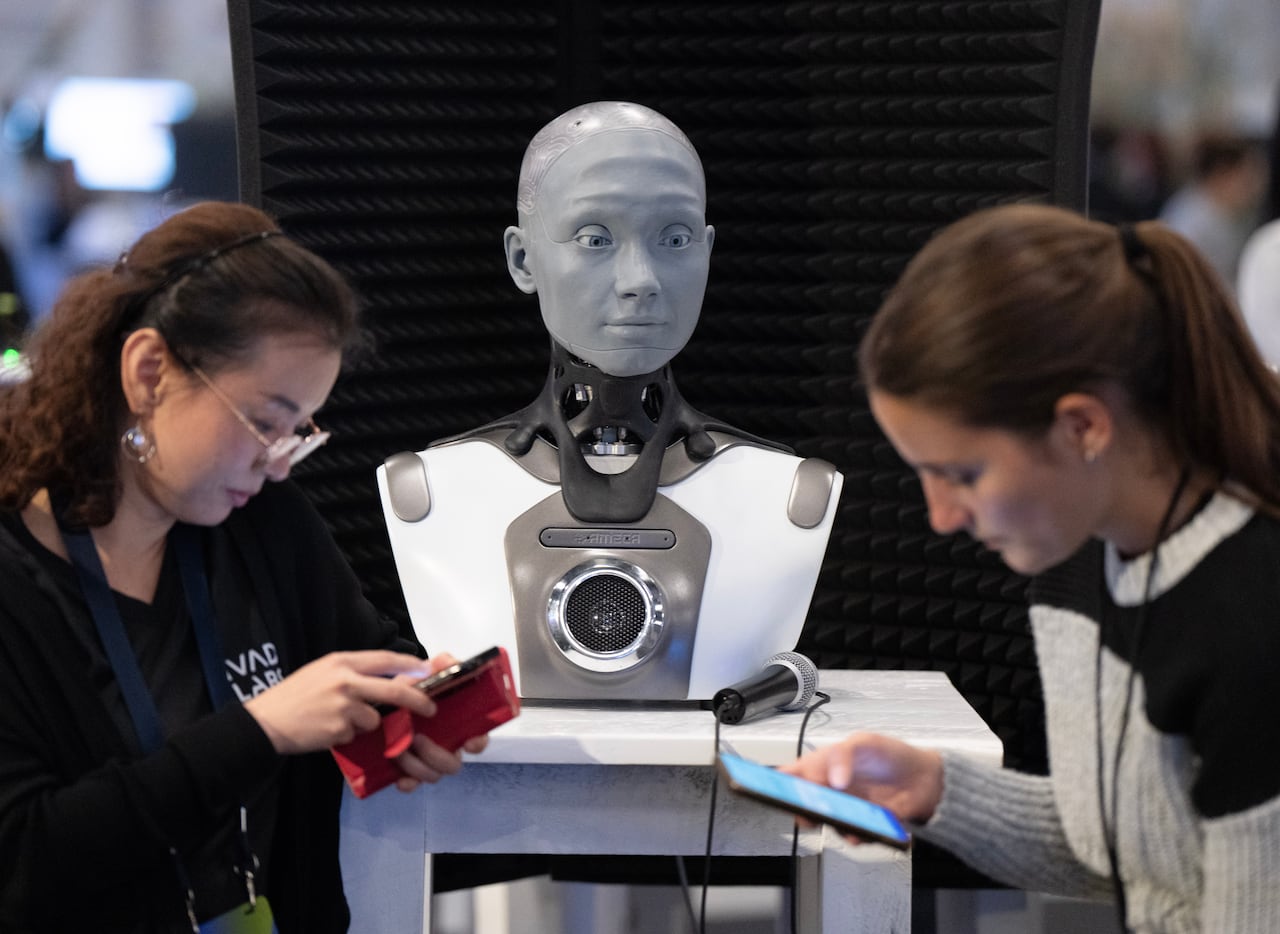 Two people stand looking at their phones in front of an Android robot.