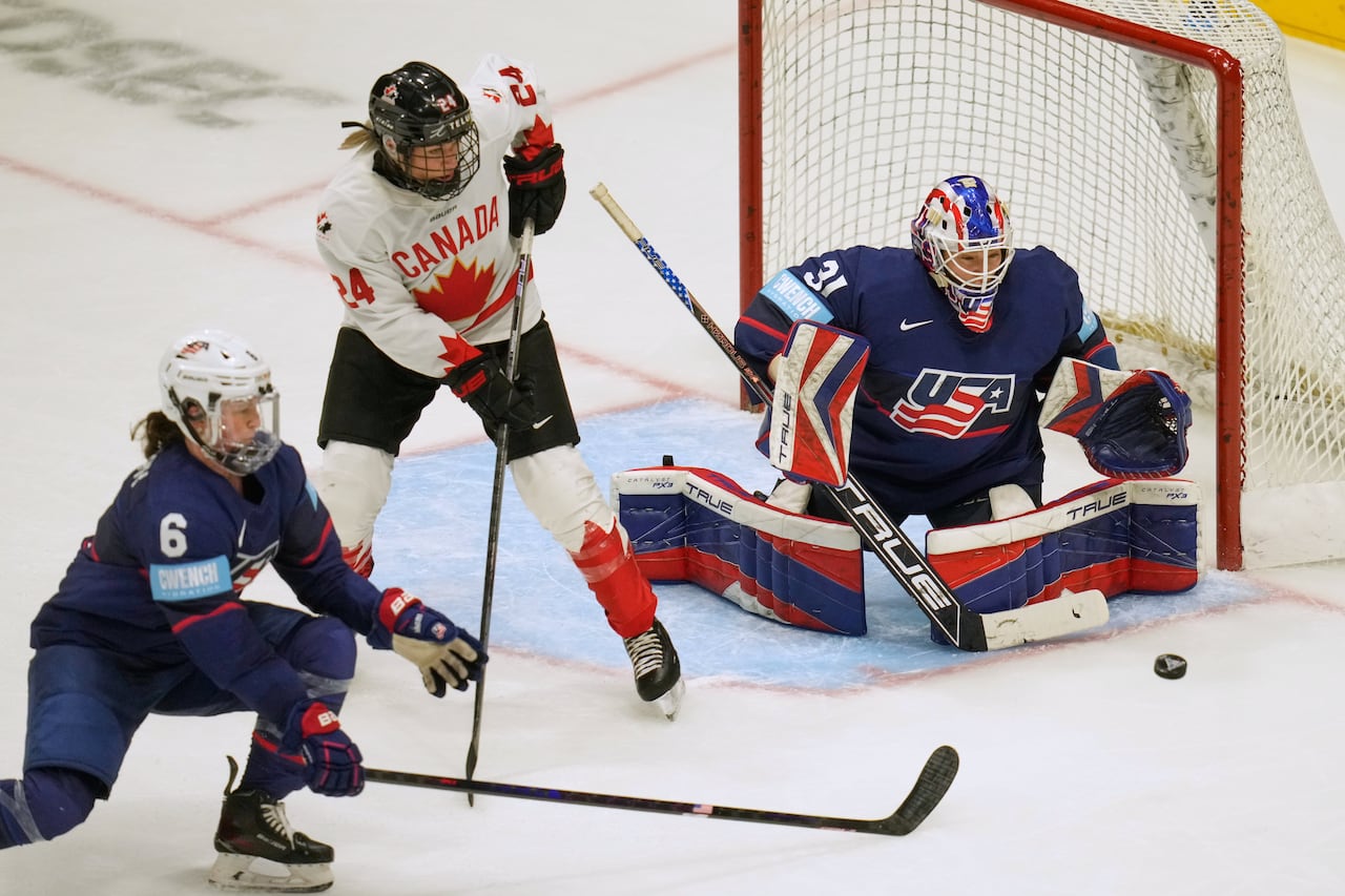 Two hockey players compete for a puck in front of a goaltender.
