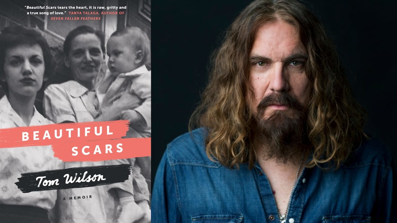 A black and white photo of two women holding a baby and leaning against a stone building. 