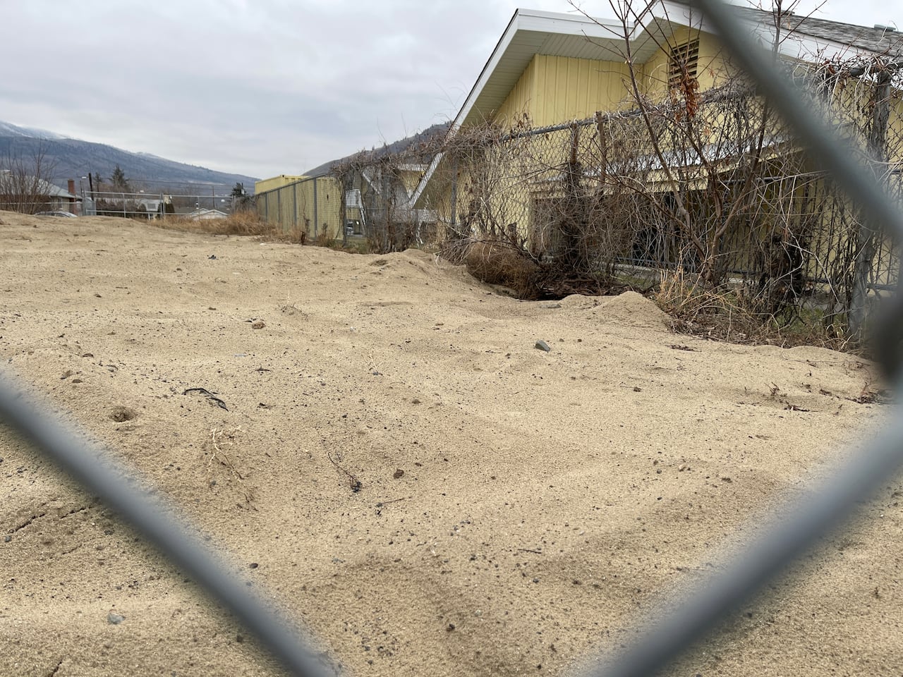 a pile of sand beside a yellow building as seen through a chain-link fence