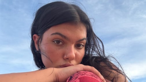 A woman sitting on a beach looks at the camera