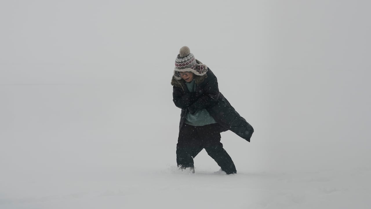 A person is seen amid snow, bracing against strong wind.
