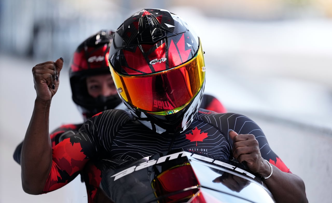 A women's bobsleigh team raises their fists in reaction after a run.