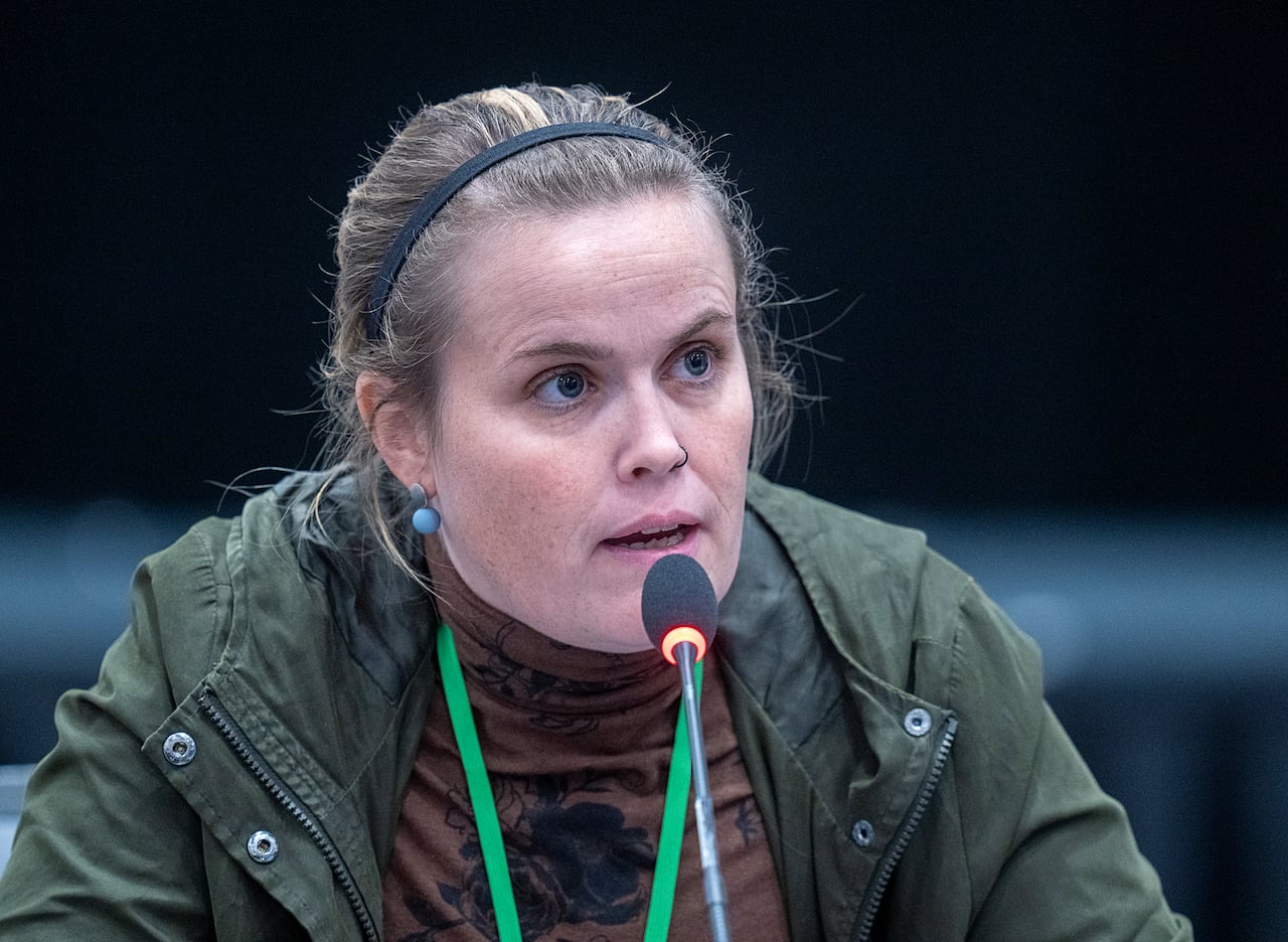 A woman in a green jacket speaks into a microphone.