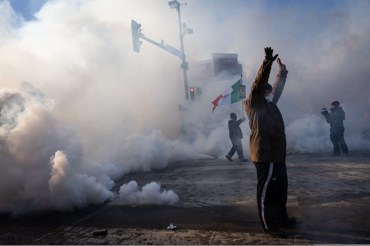 Protesters hold up their hands as smoke rises.