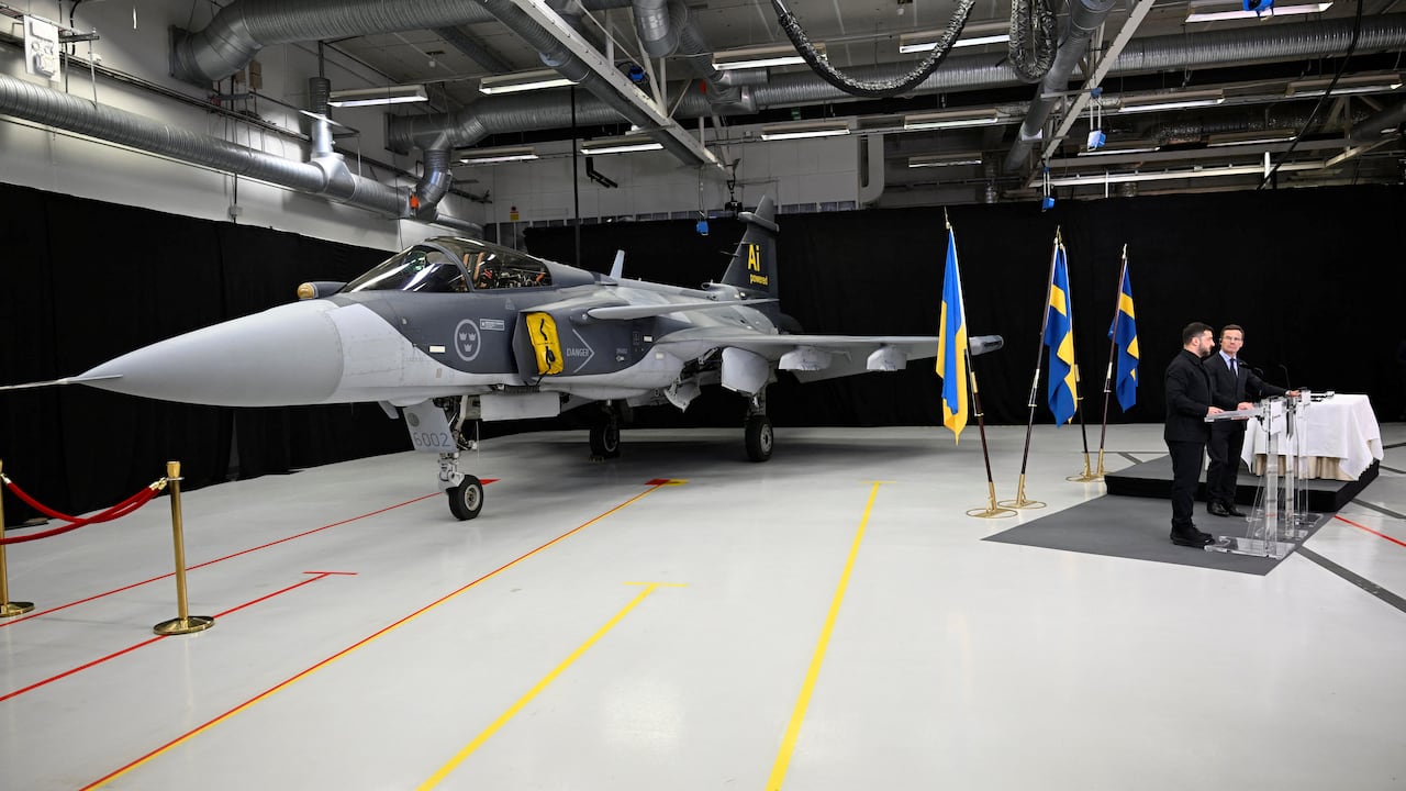 a jet inside a hanger, with yellow and blue flags nearby