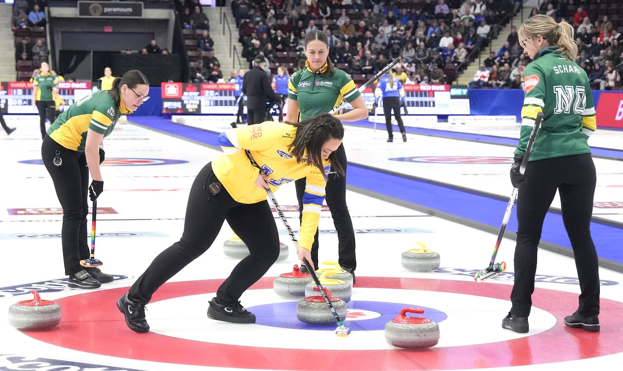 A skip representing Alberta brushes a curling stone away.