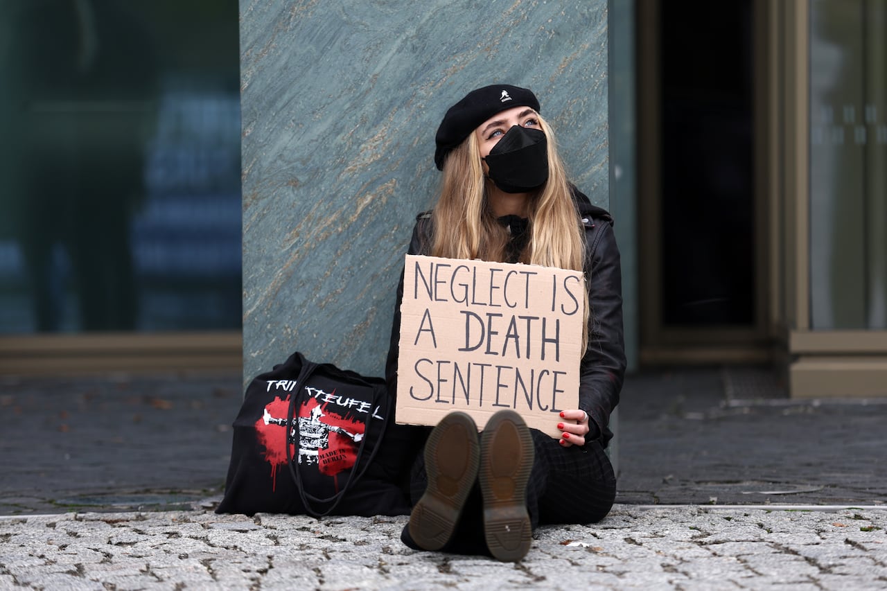 A protester wearing a medical mask holds a placard reading "Neglect is a death sentence"
