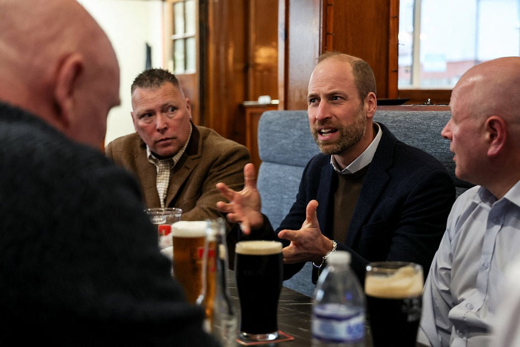 Several adults sit at a table in a pub with full pints of beer in front of them.