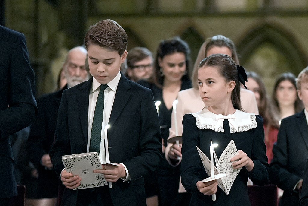 One child looks at another child as they stand during a carol service and hold programs and candles.