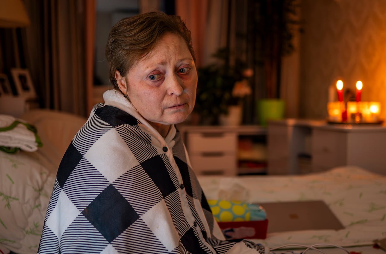 A woman is wrapped in a black and white blanket in a room lit with candles.