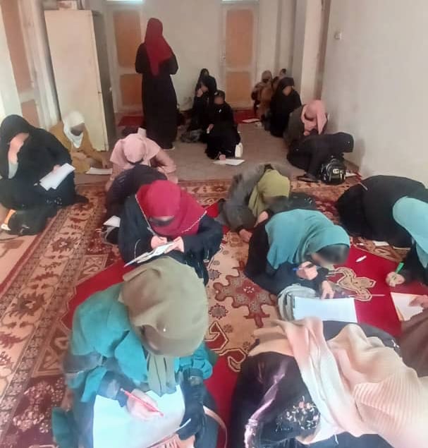 Girls sit on a floor while a teacher