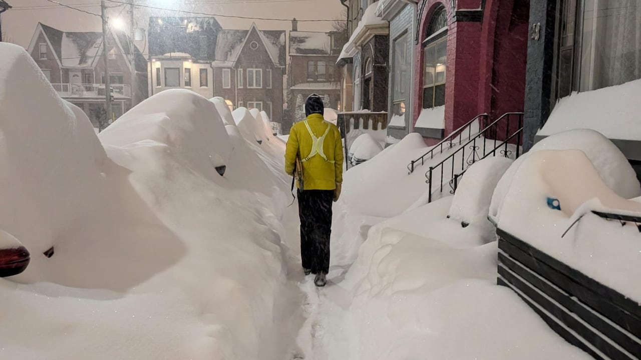 Heavy snow covers sidewalks and a row of cars in Toronto's west end at night.