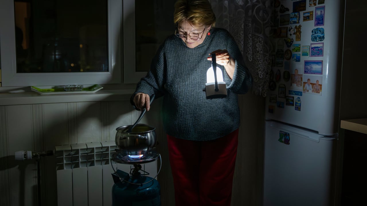 A woman holding a lamp cooks over a small heating device.