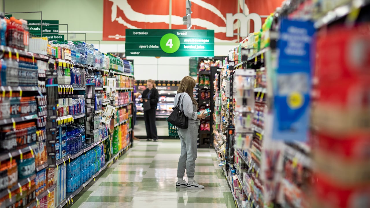 An individual looks at a product box in a supermarket aisle. 