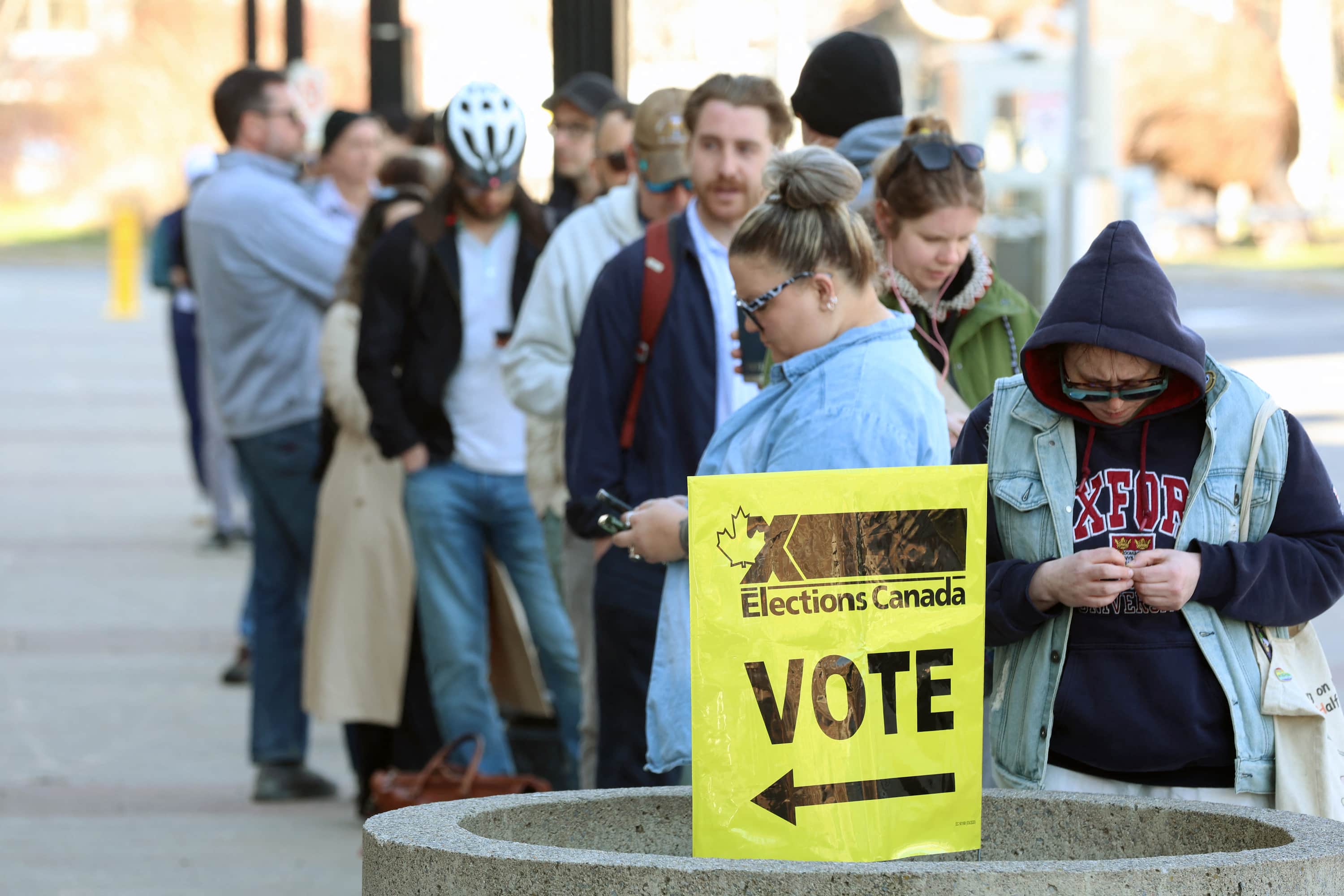People stand in line behind an Elections Canada Vote sign.